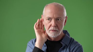 Gri sakallı olgun bir adam, parlak yeşil bir ekrana karşı, dikkatlice dinlerken el kol hareketi yapar. Onun ifadesi bu stüdyo ortamında merak ya da şaşkınlık gösteriyor..