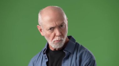 Olgun bir adam yeşil bir ekranın önünde kaslı vücudunu sergileyerek kolunu esnetir. Üzerinde kot gömlek ve siyah gömlek olan sıradan bir kıyafet giyiyor..