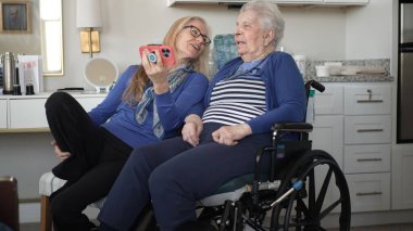 90 'lı yaşlarda bir kadın, kızıyla evde keyifli bir görüntülü sohbet etmekten hoşlanır. Kahkahaları paylaşıyorlar ve sıcak ve destekleyici bir ortamda sevgi dolu anılar yaratıyorlar..