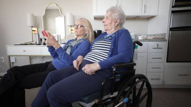 Tekerlekli sandalyedeki yaşlı bir kadın evde kızıyla samimi anlar yaşıyor, akıllı telefon kullanarak bağlı kalıyor ve birlikte anılara değer veriyor..