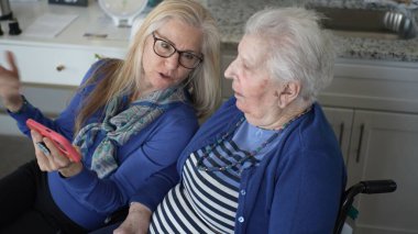 Bir kız, evde rahat bir ortamda yaşlı annesiyle iletişim kurar, fotoğraflara bakmak ve hatıralarını paylaşmak için akıllı bir telefon kullanır, birlikte geçirdikleri güzel anları ön plana çıkarır..