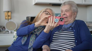 90 'lı yaşlarda yaşlı bir kadın akıllı telefon kullanırken kızıyla samimi bir anı paylaşıyor. Kapalı alandalar, birlikte güzel anılar yaratıyorlar..