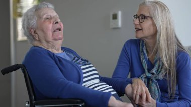 Yaşlı bir kadın ve kızı arasındaki sıcak etkileşim, kapalı bir ortamda. Birlikte geçirdikleri her gün boyunca sevgi ve ilgi gösterirler..