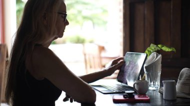 Olgun bir kadın bir kafede oturur, bir fincan kahvenin tadını çıkarırken tablet kullanır. Atmosfer sakin ve iş için elverişli..