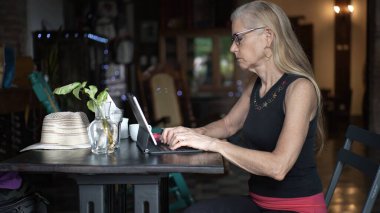 Yetişkin bir kadın kafede tablet kullanır. Telefonuyla işine odaklanır. Rahat bir ortamda dijital göçebe yaşam tarzını benimsiyor..