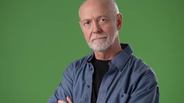 Sakallı ve kısa saçlı, kolları çapraz duran, kendinden emin bir ifade sergileyen olgun bir adam. Siyah bir gömleğin üstüne düğmeli bir gömlek giyer..