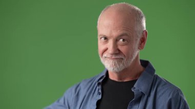 Orta yaşlı, sakallı bir adam başparmağını kaldırırken sıcak bir şekilde gülümsüyor. Parlak yeşil bir arka planın önünde, neşeli bir atmosfer yaratıyor..