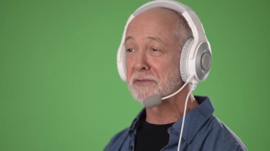 Neşeli bir ifadeye sahip orta yaşlı bir adam yeşil ekran arkaplanı önünde kulaklık takıyor..