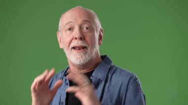 Sakallı olgun bir adam, elleri havada el kol hareketi yaparak heyecan ve şaşkınlık gösterir. Yeşil ekranlı bir stüdyo ortamında fotoğraf çekiliyor..