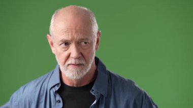 Sakallı olgun bir adam, parmakları dudaklarında, canlı yeşil bir ekran arkaplanında tasvir edilmiş, sessiz bir jest yapıyor..