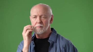 Gri saçlı ve sakallı olgun bir adam gözlerini kapar, elini yüzüne koyar ve derin düşüncelere dalmış parlak yeşil bir zemin üzerinde durur..