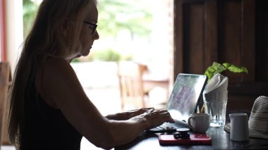 Sıcak bir kafede, olgun bir kadın bilgisayarını ve tabletini kullanarak kahvesini yudumlayarak dijital göçebe yaşam tarzını somutlaştırıyor..