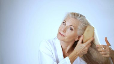 Sakin bir spa ortamında, olgun bir kadın makyaj yaparken mutlu bir şekilde gülümser. Rahatlamış tavrı memnuniyeti ve özgüvenini parlak, beyaz bir arka planda yansıtıyor..