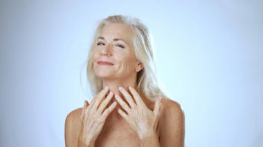 Sakin bir spa ortamında, olgun bir kadın kendini şımartırken mutlu bir şekilde gülümser, rahat ve memnun bir tavırla cilt bakımı uygular..