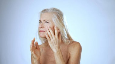 Olgun bir kadın spa tedavisi görüyor. Cilt bakımına odaklanırken gülümsüyor. Sakin, aydınlık bir yerde..