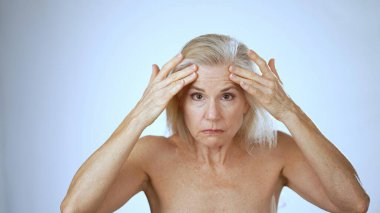 Olgun bir kadın huzurlu bir spa ortamında oturur, boynuna masaj yaparken mutlu bir şekilde gülümser, rahatlama ve memnuniyet havası yayar..