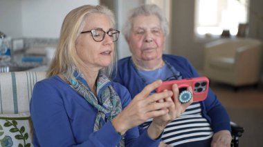 Kapalı bir ortamda, bir kadın yaşlı annesine tekerlekli sandalyede destek olur. Yürekten bir ziyaret sırasında akıllı telefondan anılarını paylaşırlar..