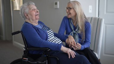 Bir kız çocuğu, tekerlekli sandalyedeki yaşlı annesiyle keyifli bir şekilde iletişim kurar. Evlerinde sevgi ve ilgi dolu bir anı paylaşır..