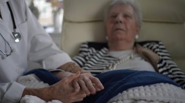 Yaşlı bir kadın evinde dinlenirken, bir sağlık görevlisinden şefkatli bir ziyaret alıyor, etkileşim sırasında konfor ve bakımı teşvik ediyor..