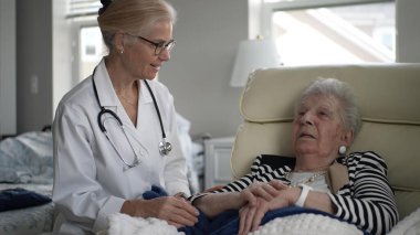 Olgun bir kadın rahat bir sandalyede dinlenirken bir sağlık uzmanı ev ziyareti sırasında sağlığını dikkatle kontrol ediyor ve rahatlatıcı bir atmosferi teşvik ediyor..