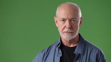 Sakallı olgun bir adam, bir el hareketini kendine güvenle kaldırır. Parlak yeşil bir ekranın önünde poz veriyor, anlamlı varlığını arttırıyor..