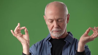 Olgun bir adam, gözleri kapalı meditasyon yapıyor, elleri sakin bir jest ile kaldırılıyor, canlı yeşil bir perde arkasına kuruluyor..