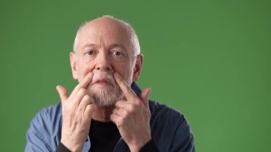 Gri saçlı ve sakallı olgun bir adam saçını düzeltirken şaşırır. Parlak yeşil bir ekrana yaslanmış, canlı bir atmosfer yaratıyor..