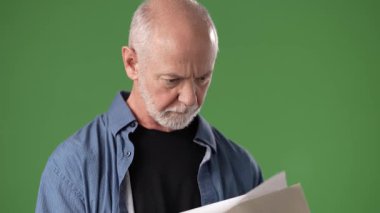 Neşeli bir ifadeye sahip olgun bir adam elinde birkaç sayfa kağıt tutarak yeşil ekranın önünde canlı bir tartışma ya da sunumla meşgul oluyor..