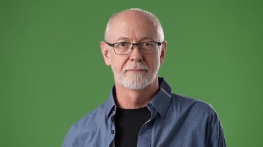 Gözlüklü ve sakallı orta yaşlı bir adam yeşil ekranın önünde güvenli bir şekilde poz veriyor, siyah bir tişört giyip projeye hazırlanıyor..