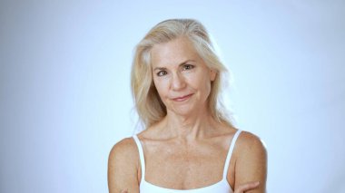 Uzun açık renk saçlı olgun bir kadın spa ortamının keyfini çıkarırken mutlu bir şekilde gülümsüyor. Temiz beyaz bir arka plana karşı rahatlık ve memnuniyet yayıyor..