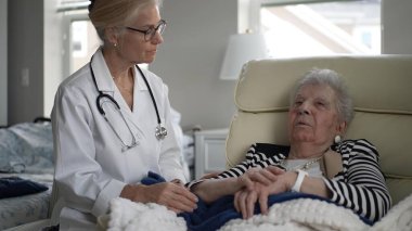 Bir hemşire, evinde yaşlı bir kadınla dikkatlice temas kurar, ziyaret sırasında tıbbi destek ve arkadaşlık sağlar, konfor ve bakımı teşvik eder..