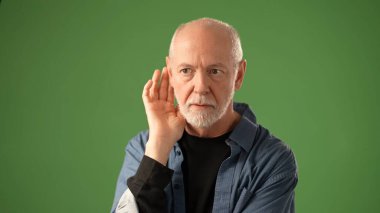 Olgun bir adam, düşünceli bir ifadeyle ve bir sırrı saklama önerisiyle, katı yeşil bir ekran arkaplanına karşı, portre oturumu sırasında bir anlık tefekkür ve duygu sergiliyor..