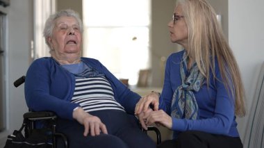 90 'lı yaşlarda yaşlı bir kadın, yakın ilişkilerinin altını çizen samimi bir ziyaret sırasında kızından destek ve sevgi alarak tekerlekli sandalyede oturuyor..