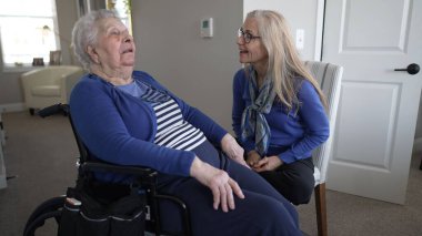 90 'lı yaşlarda bir kadın evinde tekerlekli sandalyede otururken, kızı onunla özen ve sevgiyle konuşuyor, yakın bağlarını ve günlük yaşamlarını vurguluyor..