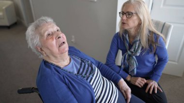 90 'lı yaşlarda yaşlı bir kadın sevgi dolu sıcak bir aile ziyareti sırasında evinde tekerlekli sandalyede oturuyor ve kızından ilgi görüyor..