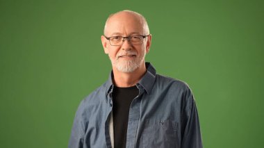 Sakallı ve gözlüklü olgun bir adam, parlak bir gülümseme sergiliyor. Saf yeşil bir zemin üzerinde, coşkulu bir sevinç ve sıcaklık yayıyor..