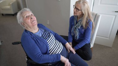 Ev ortamında, 90 'lı yaşlarda bir kadın tekerlekli sandalyede otururken, kızı aile ziyareti sırasında arkadaşlık, ilgi ve sevgi sunuyor..