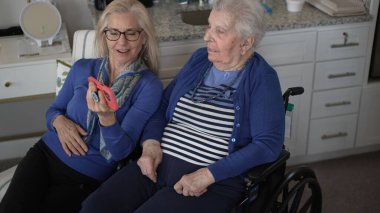Tekerlekli sandalyedeki yaşlı bir kadın kızıyla görüntülü sohbetten zevk alıyor. Evlerinde samimi bir ziyaret sırasında sevgi ve hatıralar besliyor..