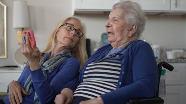 Tekerlekli sandalyedeki yaşlı bir kadın kızıyla görüntülü konuşma yapar, sıcak bir ev ortamında neşeli anılar yakalar..