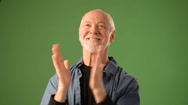 Açık sakallı son sınıf öğrencisi parlak yeşil bir arka planın önünde dururken kurnazca gülümsüyor. Giysileri, duyguları ve sıcaklığı yansıtan günlük bir gömlekten oluşuyor..