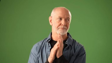 Neşeli bir gülümsemesi olan olgun bir adam ellerini katı yeşil bir ekranın önünde çırpıyor. Duyguları bir kutlama anında mutluluk ve bağlılık iletir..