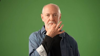 Dostane bir gülümsemesi olan kıdemli bir adam yeşil bir ekrana karşı duruyor, sıcaklığı ve güveni var. Sıradan bir kıyafet giyiyor, rahat bir tavır sergiliyor..