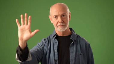 Kıdemli adam katı yeşil bir ekranın önünde duruyor, elini kullanarak dur ve duygularını ifade et diyor, dikkat ve bağlılık çeken etkileyici bir portre oluşturuyor..