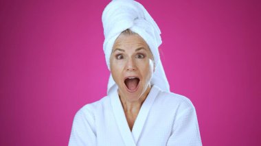 Olgun bir kadın spa ortamında mutlu bir şekilde gülümser, fırçayla makyaj yapar. Huzurlu beyaz arka plan onun neşeli ifadesini ve kişisel bakımını arttırır..