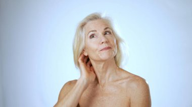 Neşeli, olgun bir kadın spa 'da huzur içinde, mutlu bir şekilde gülümserken sakin, aydınlık bir ortamda kendi başının çaresine bakıyor..