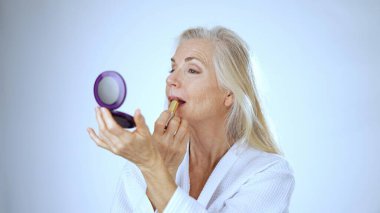 Olgun bir kadın spa 'da cilt bakımı yaparken sevinçle gülümser. Rahatlatıcı beyaz arka plan onun gevşemiş ve neşeli ifadesini arttırır..