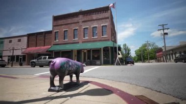 Cadiz, KY, ABD - 04 26 2025: Cadiz, Kentucky şehir merkezindeki köşede yerel cazibe ve sanat eserlerini sergileyen renkli domuz heykeli bulunuyor. Tuğla binalar ve temiz gökyüzü atmosferi güçlendirir..