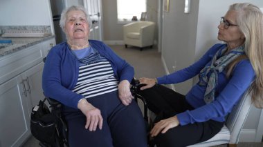 Kapalı bir ortamda, 90 'lı yaşlarda yaşlı bir kadın tekerlekli sandalyede oturuyor. Kızı ziyaret sırasında sevgi ve destek sağlıyor, bağlarını vurguluyor..