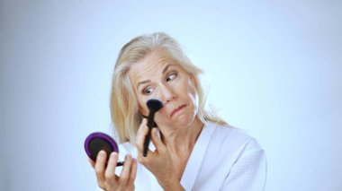 Uzun, açık renk saçlı mutlu bir kadın, sakin bir spa ortamında yumuşak bir bornoz giyerken parlak bir şekilde gülümser. Sakin beyaz arka plan onun neşeli yüz ifadesini arttırır..