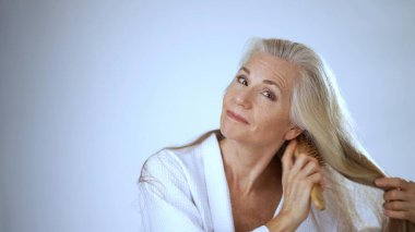 Spa bornozu giymiş olgun bir kadın, huzur içinde gülümserken etrafını huzur dolu, beyaz bir arka plan sarmış, tipik bir sağlık merkezi gibi..